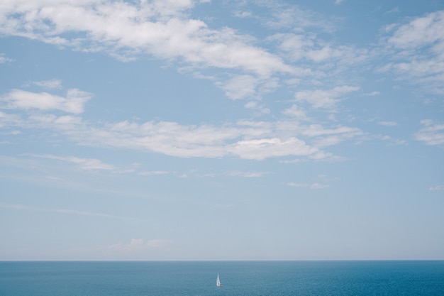 Un velero solitario flota en la distancia en aguas tranquilas, cielo azul. El concepto de libertad y facilidad.