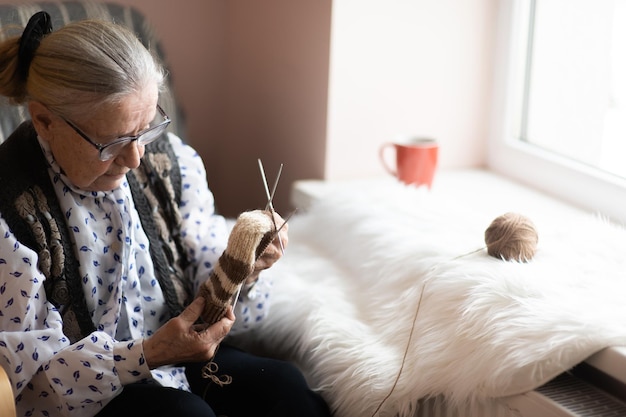 Velha tricotando em um lar de idosos perto da janela