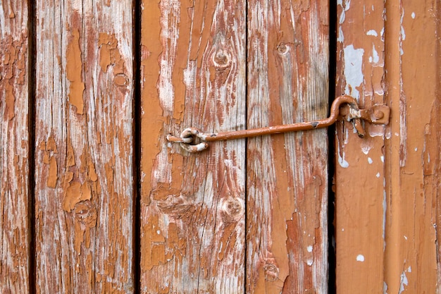 Velhas dobradiças enferrujadas na porta rachada de madeira marrom fecham