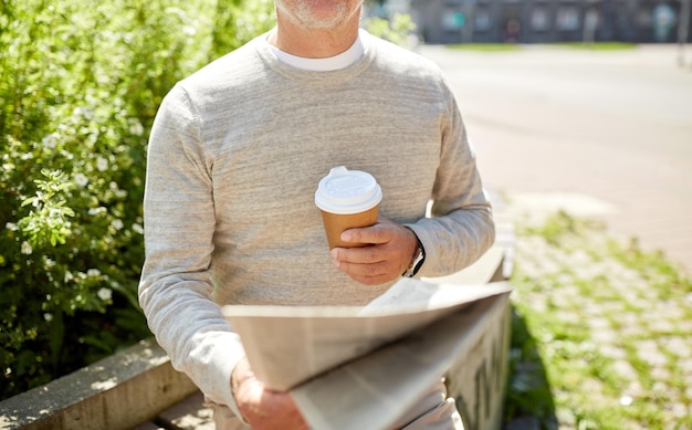 velhice e conceito de pessoas - homem sênior com café lendo jornal sentado no banco da rua