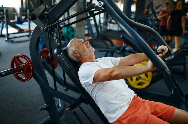 Velho alegre na máquina de exercícios na academia