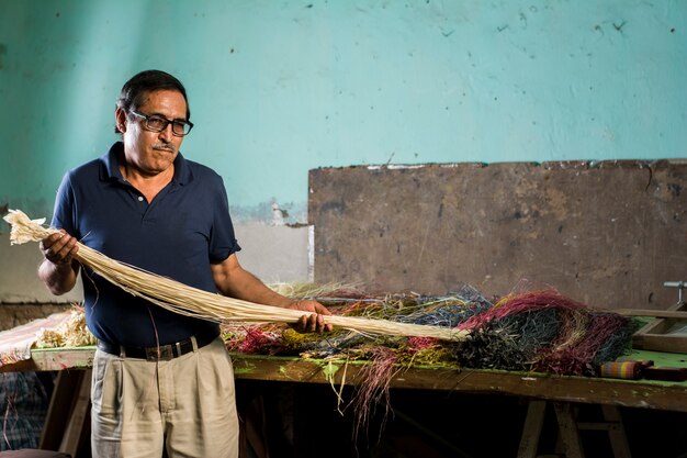 velho artesão latino-americano tecendo com as mãos mostrando suas ferramentas e materiais