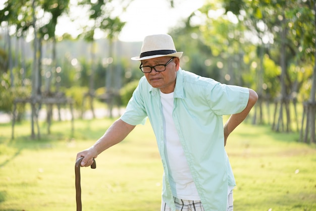 Velho asiático andando no parque e com uma dor nas costas