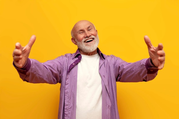 Velho avô careca em camisa roxa puxa as mãos para a frente e abraços em fundo isolado amarelo