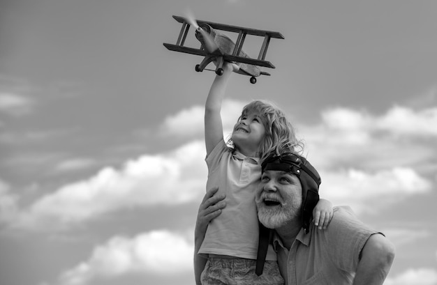 Velho avô e neto brincando com avião de brinquedo contra o fundo do céu de verão