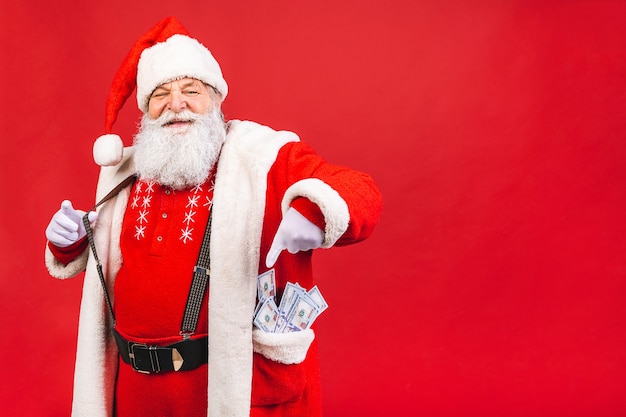 velho barbudo fantasiado de Papai Noel com dinheiro no bolso, isolado no fundo vermelho