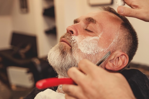 velho barbudo sendo barbeado em uma barbearia Classic shave by Stainless Steel Straight Edge Razor