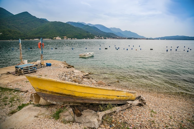 Velho barco amarelo na costa perto da fazenda de mexilhões e ostras ao longo da costa da Baía de Kotor