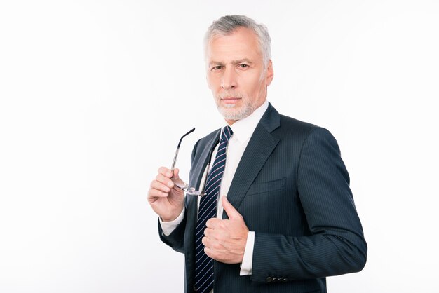 Velho bonito em um terno de negócios segurando óculos e gesticulando com o polegar para cima