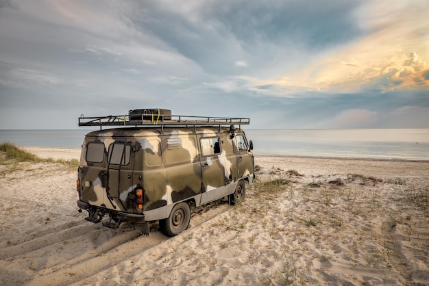 Velho carro militar na areia da praia ao pôr do sol