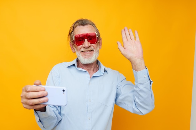 Velho em óculos vermelhos na moda com um telefone de fundo amarelo