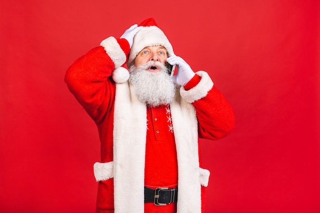 Velho fantasiado de papai noel falando em um telefone celular isolado sobre fundo vermelho