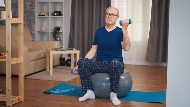 Velho fazendo treinamento de bíceps com halteres na bola de estabilidade. idoso reformado treino saudável saúde desporto em casa, exercício de actividade física na velhice