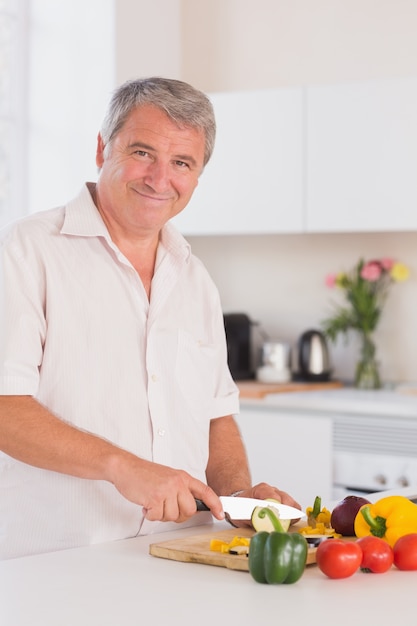 Velho homem sorrindo e cortando vegetais