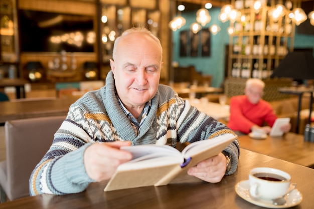 Velho, lendo um livro em um café