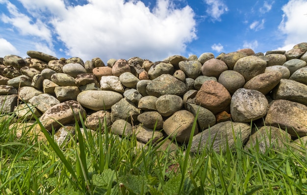 Velho muro de pedra com grama verde na frente e céu azul com nuvens acima