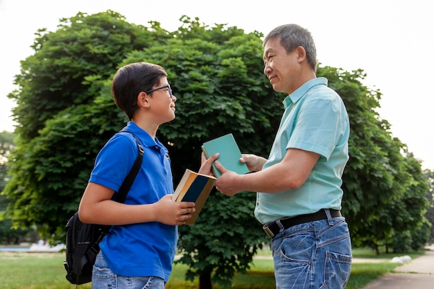 Velho pai asiático vai para a escola com filho e carrega livros menino coreano com mochila vai para a escola