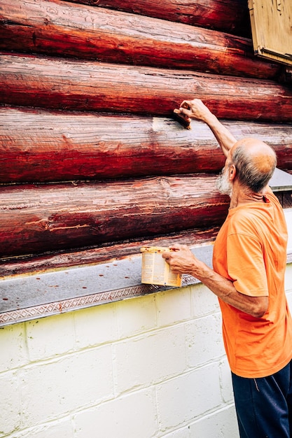 Velho pintando a parede da casa do lado de fora do carpinteiro masculino sênior aplicando verniz protetor ou tinta para pr
