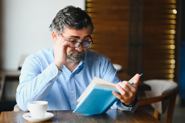 Velho sênior lendo um livro em uma cafeteria desfrutando de seu hobby literário