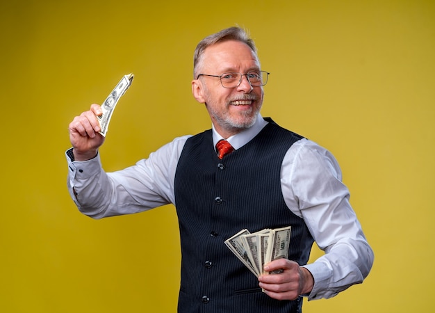 Velho sorridente homem de cabelos grisalhos em óculos, segurando um leque de dólares na mão.