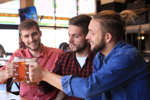 Velhos amigos alegres se divertindo e bebendo cerveja no balcão do bar no pub.