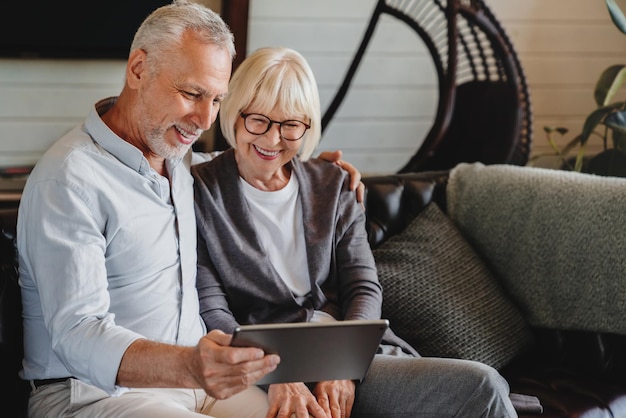 Velhos pensionistas homem e mulher sorrindo e descansando no sofá com computador tablet