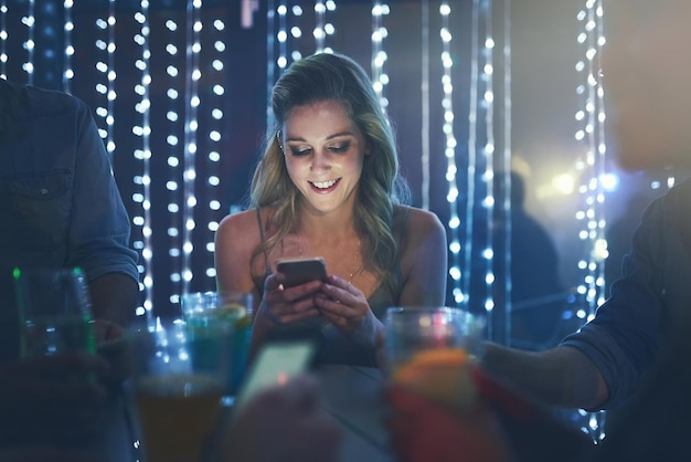 Ven aquí ahora, esta fiesta es increíble Foto de una mujer joven que envía mensajes de texto en su teléfono inteligente mientras está sentada en un club nocturno lleno de gente