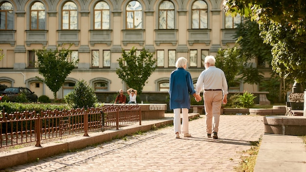 Foto ven conmigo vista posterior de la pareja de ancianos tomados de la mano mientras caminan juntos al aire libre