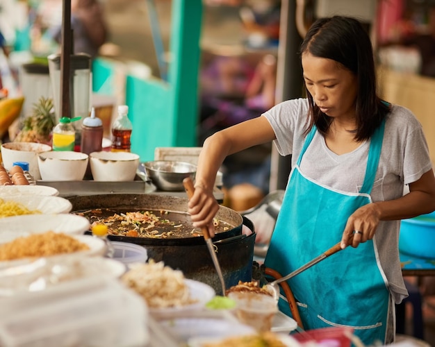 Ven y tómalo Foto de un vendedor de alimentos que prepara un plato tailandés en un mercado de alimentos