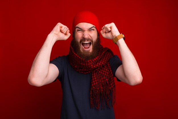 Vencedor com raiva, barbudo, vestindo roupas quentes e comemorando com os braços para cima e gritando com câmera