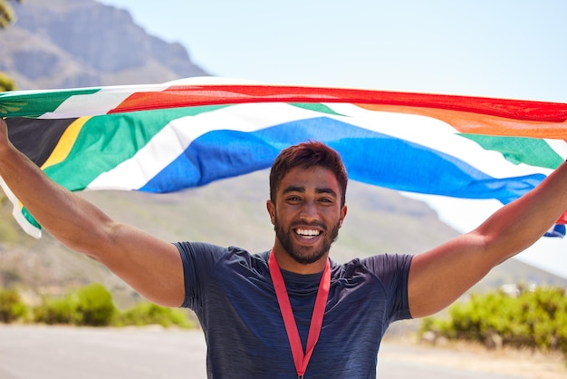 Vencedor do corredor e retrato de homem feliz com bandeira na estrada para vitória de objetivo de fitness ou corrida de corrida Campeão esportivo orgulhoso sul-africano ou atleta animado com vitória ou sucesso na competição