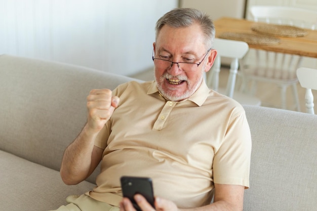 Vencedor eufórico de homem sênior de meia-idade com smartphone, avô maduro mais velho, olhando para o telefone celular
