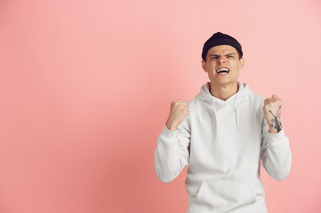 Vencedor louco e feliz. Retrato moderno de jovem caucasiano isolado no fundo rosa do estúdio. Lindo modelo masculino em branco. Conceito de emoções humanas, expressão facial, vendas, anúncio. Copyspace.