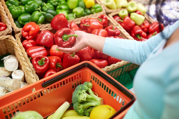 venda, compras, alimentos, consumismo e conceito de pessoas - mulher com cesta comprando pimentas ou pimentão na mercearia