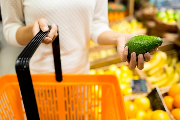 venda, compras, consumismo e conceito de pessoas - close-up de jovem com cesta de alimentos e abacate no mercado