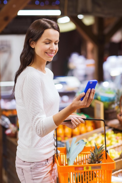 Foto venda, compras, consumismo e conceito de pessoas - jovem feliz com cesta de alimentos e smartphone no mercado