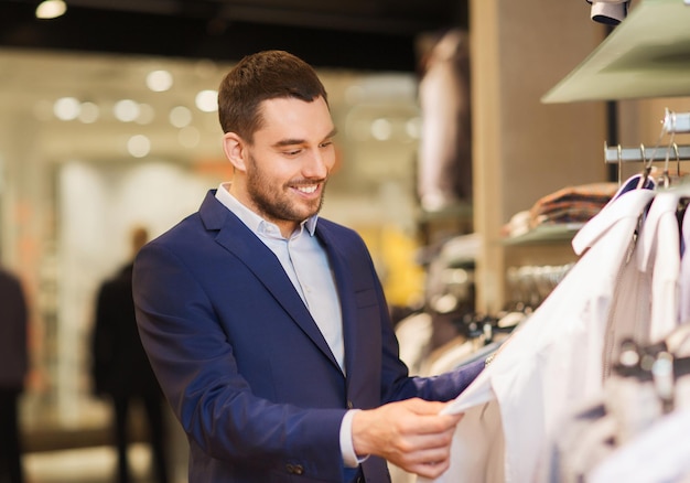 Foto venda, compras, moda, estilo e conceito de pessoas - jovem elegante de terno escolhendo roupas no shopping ou loja de roupas