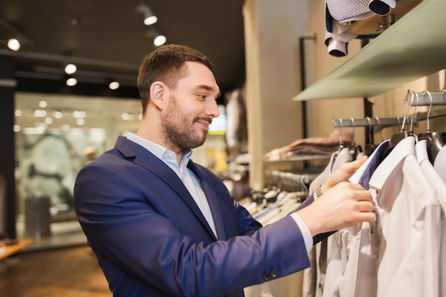 venda, compras, moda, estilo e conceito de pessoas - jovem elegante de terno escolhendo roupas no shopping ou loja de roupas