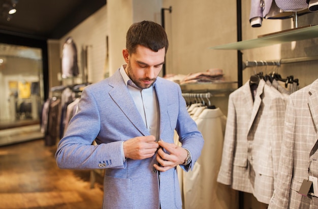 venda, compras, moda, estilo e conceito de pessoas - jovem elegante escolhendo e experimentando jaqueta no shopping ou loja de roupas