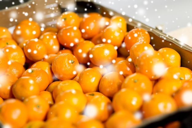 venda, compras, vitamina c e conceito de comida saudável - tangerinas maduras no mercado ou fazenda sobre efeito de neve