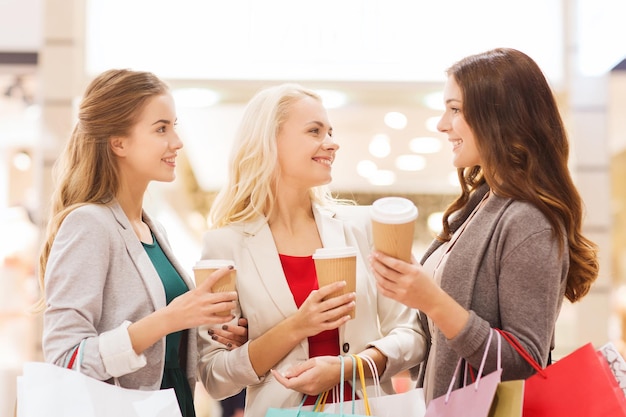 Venda, consumismo e conceito de pessoas - mulheres jovens felizes com sacolas de compras e xícara de papel de café no shopping