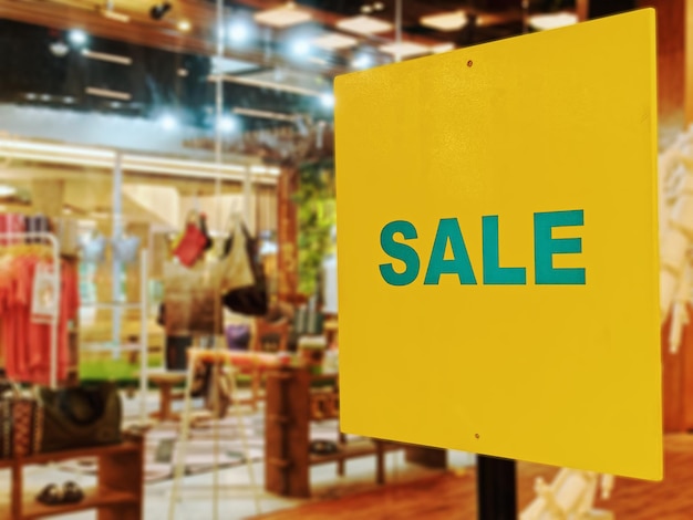 Foto venda de texto promocional em etiqueta amarela contra fundo desfocado de loja de roupas