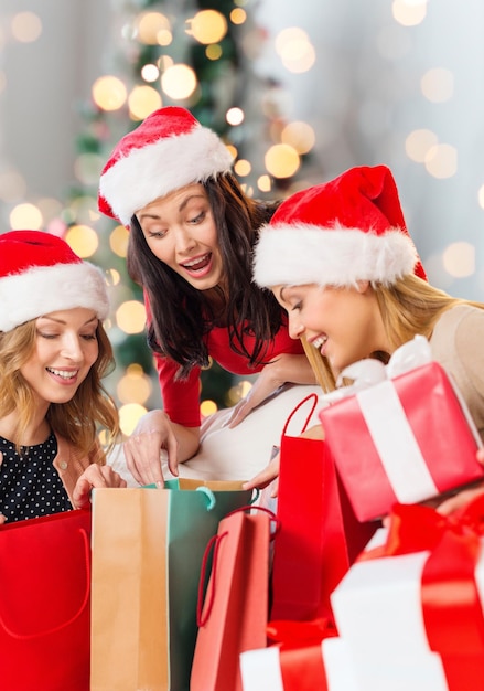 venda, férias de inverno e conceito de pessoas - jovem sorridente no chapéu de ajudante de papai noel com presentes e sacolas de compras sobre fundo de luzes da árvore de natal