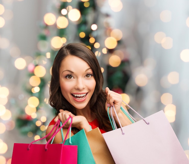 venda, presentes, feriados e conceito de pessoas - mulher sorridente com sacolas coloridas sobre a sala de estar e o fundo da árvore de natal