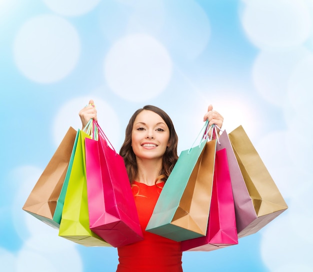 Foto venda, presentes, natal, feriados e conceito de pessoas - mulher sorridente com sacolas coloridas sobre fundo de luzes azuis