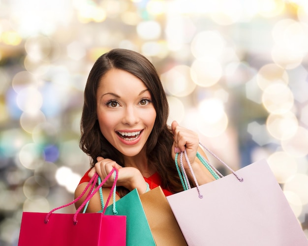 venda, presentes, natal, feriados e conceito de pessoas - mulher sorridente com sacolas coloridas sobre fundo de luzes