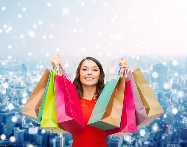 venda, presentes, natal, feriados e conceito de pessoas - mulher sorridente com sacolas coloridas sobre o fundo da cidade de neve