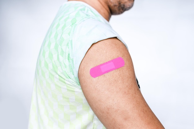 Un vendaje rosado está unido al brazo del hombre Concepto de primeros auxilios después de la vacunación contra el coronavirus COVID-19 y la aguja médica profesional cáncer de sangre Closeup fondo borroso blanco