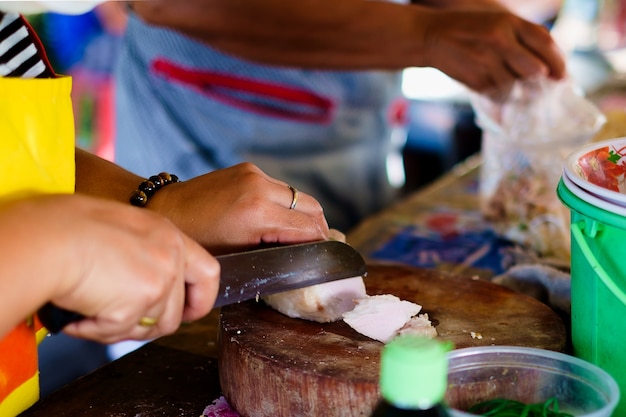 Vendedor ambulante femenino que corta la carne de cerdo para cocinar