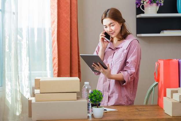 El vendedor asiático en línea trabaja en casa hablando con el cliente por teléfono